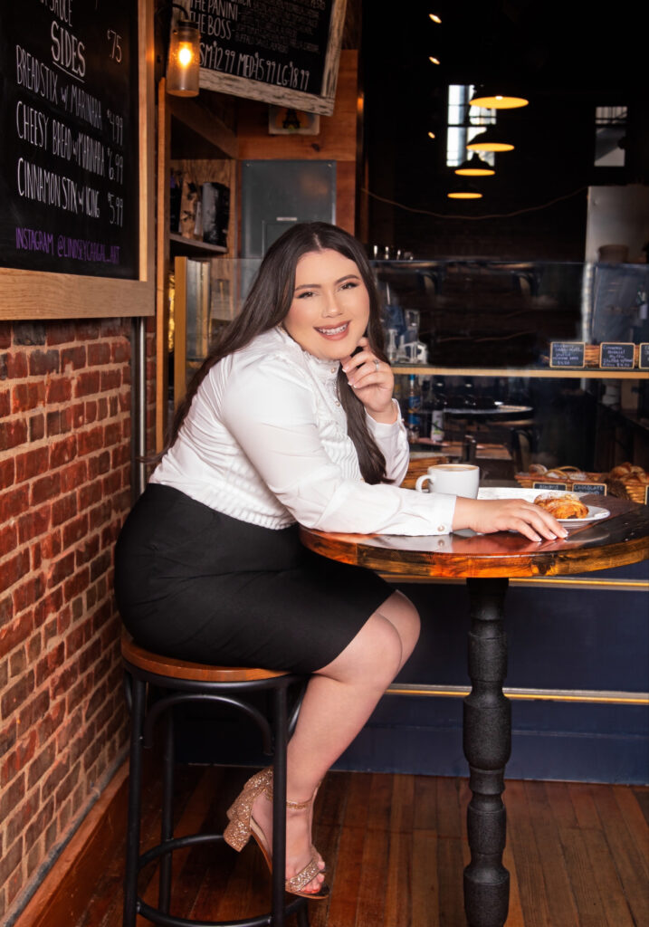 Woman in white top and black skirt sits at cafe table.