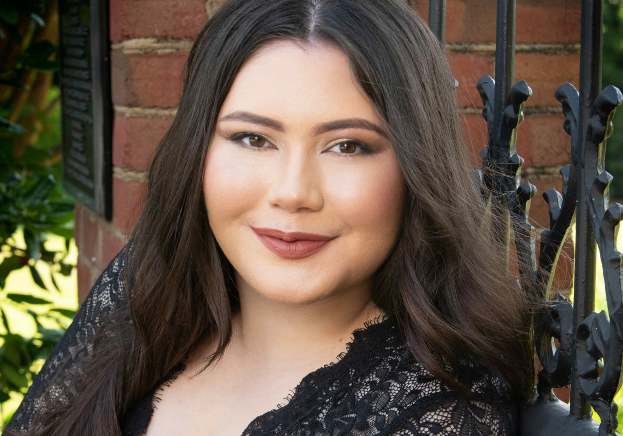 Woman in black lace dress leaning against iron fence.